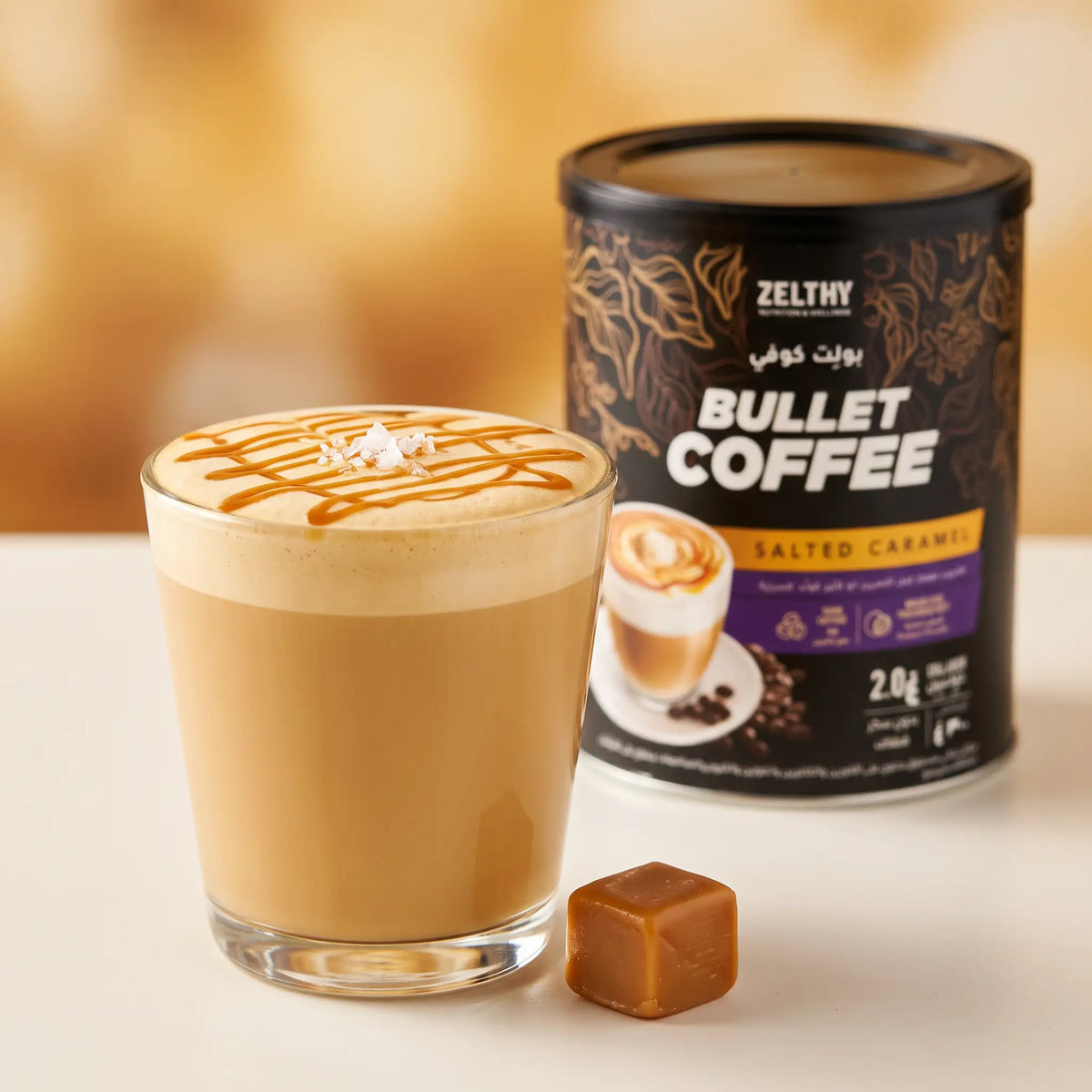 A creamy coffee topped with caramel drizzle and salt flakes beside a tin of Zelthy Bullet Coffee Salted Caramel