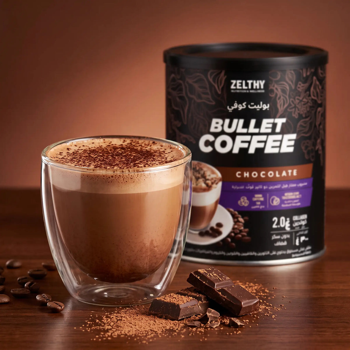 A creamy mocha dusted with cocoa beside a tin of Zelthy Bullet Coffee Chocolate and pieces of dark chocolate