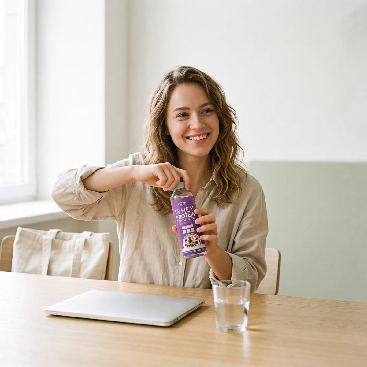 A young woman at a table opening a Zelthy Whey Protein single-serve bottle, a glass of water beside her